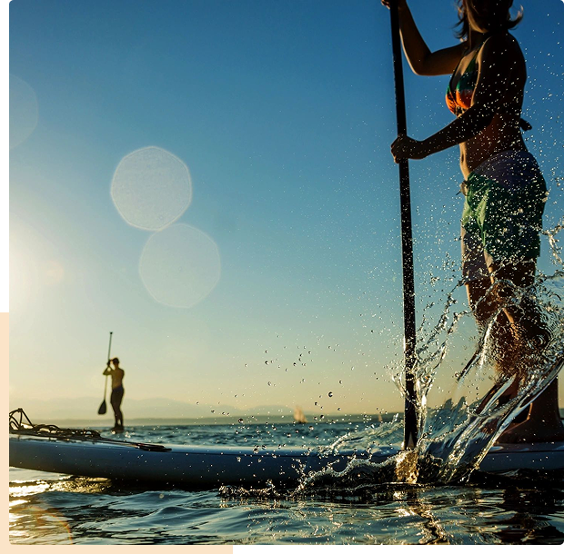 People paddleboarding on water during sunset with splashes around.